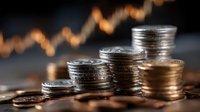 Stacks of silver and gold coins with blurred financial chart showing upward trend in background representing investment growth and wealth accumulation.