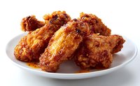 Crispy fried chicken wings with spicy honey glaze sauce served on white plate, close up view of golden brown, crunchy coating and juicy meat.