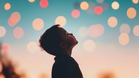 Young African American boy silhouette against sunset sky with dreamy bokeh lights, looking up with wonder and hope. Peaceful childhood moment capturing imagination and dreams.