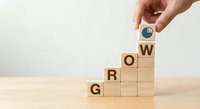 Hand placing circular chart icon on wooden blocks spelling GROW representing business growth strategy and development progress on neutral background.