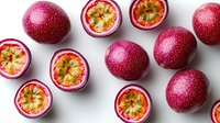 Fresh passion fruits cut in half showing juicy pulp and seeds with whole ripe purple passion fruits on white background, top view food photography.