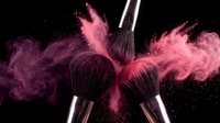 Professional makeup brushes with pink powder explosion on black background for cosmetic advertising and beauty industry campaigns.