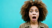 Young African American woman with curly afro hair showing shocked surprised expression with open mouth against bright turquoise background for advertising campaigns.