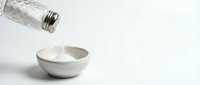 Milk pouring from glass bottle into ceramic bowl on white background for dairy product advertising and kitchen photography.