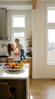 Young Caucasian mother holding toddler son in bright modern kitchen with fresh fruit bowl on white marble island counter for family lifestyle content.