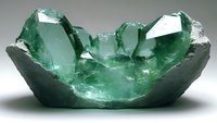 Raw emerald crystals growing in dark matrix stone formation, displaying vibrant green color and natural geometric crystalline structure with translucent properties.