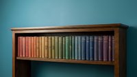Colorful book collection arranged by rainbow spectrum on wooden bookshelf against turquoise wall creating organized library display for home office decor.