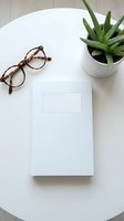 Minimalist workspace with blank white notebook, tortoiseshell eyeglasses and succulent plant on round table for business planning and creative projects.