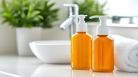 Orange cosmetic bottles with pump dispenser on white bathroom counter near towel and green plant, bright minimalist spa composition for skincare products.