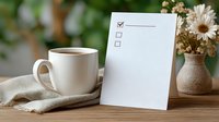 Morning coffee with checklist card on wooden table, linen napkin and dried flowers in ceramic vase against blurred green background.