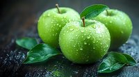 Fresh green apples with water drops and leaves on dark wooden background. Macro shot of ripe Granny Smith fruits showing natural moisture and texture.
