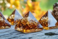 Amber orgonite pyramids with golden flakes and crystal inclusions on rustic wooden surface, glowing in sunlight against blurred natural background.