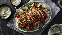 Grilled chicken breast sliced and served on fresh green salad with cherry tomatoes, red onions and creamy herb dressing on dark stone background.