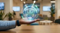 Hand holding glowing leaf hologram symbol representing sustainability, eco-friendly business, green energy innovation, and environmental responsibility in modern office workspace.