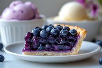 Fresh blueberry pie slice with vibrant purple filling and whole berries on top, served on white plate with ice cream scoops in background.