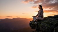 Young woman meditating on mountain cliff during golden sunset with peaceful sky and distant peaks creating serene mindfulness moment for wellness and spiritual practice.