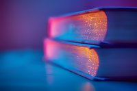 Glowing fiber optic book pages illuminated in vibrant neon pink and blue colors against dark background create magical reading atmosphere.