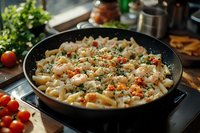 Creamy penne pasta with shrimp in garlic sauce, topped with fresh parsley and red pepper flakes, served in black skillet on wooden kitchen counter.