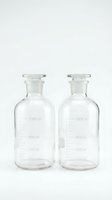 Two empty glass laboratory bottles with measurement markings and stoppers isolated on white background for scientific research and chemistry experiments.