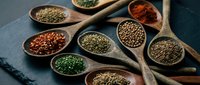 Assorted colorful spices and herbs in wooden spoons and bowls on dark slate background. Culinary ingredients for cooking and seasoning food preparation.