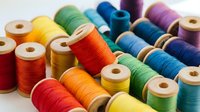 Colorful thread spools arranged for sewing and crafting projects. Vibrant cotton threads in rainbow colors on wooden bobbins for textile work and embroidery.
