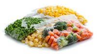 Fresh frozen vegetables in transparent plastic bags including corn, peas, broccoli and carrots arranged on white background, ready for cooking and meal preparation.