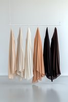 Elegant silk scarves in neutral tones hanging on minimalist white rack against light wall, showcasing gradient color palette from beige to black for fashion styling.