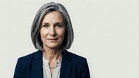 Middle-aged woman with gray hair wearing dark blazer and light blouse, professional headshot against neutral background for corporate, business, and executive portraits.