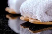 Clean white spa towels rolled on wooden bamboo mat against dark background with water drops, creating luxurious wellness atmosphere for spa treatments.