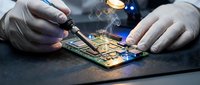 Technician in white gloves repairing smartphone motherboard with soldering iron in electronics workshop. Professional circuit board maintenance service.