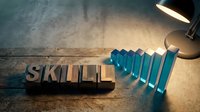 Professional development concept with wooden letter blocks spelling skill next to ascending blue bar chart under warm desk lamp light on textured surface.