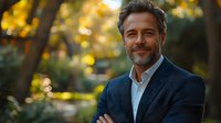 Confident mature businessman with gray beard smiling in autumn park. Professional portrait with warm golden bokeh background.