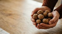 Hands holding fresh walnuts on wooden surface, suitable for food, nutrition, healthy eating, and organic product marketing materials.