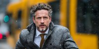 Middle-aged Caucasian businessman in gray wool coat and tie walking in snowy urban street with yellow bus background for corporate lifestyle content.