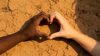 Diverse hands forming heart shape on cracked desert ground symbolizing unity, love and environmental awareness in arid landscape.