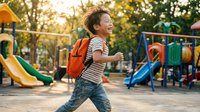 Happy young boy with orange backpack running at colorful playground during golden hour sunset, back to school concept for educational materials.