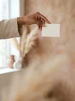 Close-up of a woman's hand holding a blank white card, wearing a beige blazer and gold bracelet, against a soft blurred background for business branding.