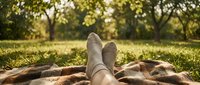 Person relaxing barefoot on blanket in sunny park with golden light filtering through trees during peaceful outdoor leisure time.