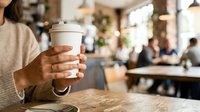 Young woman with medium skin tone holding takeaway coffee cup in casual cafe setting, ideal for beverage, lifestyle and hospitality marketing.
