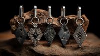 Ancient metal pendants with diamond shapes displayed on natural stone, showcasing tribal patterns and rustic textures against dark background.