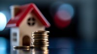 Stack of gold coins next to miniature house model on dark background with bokeh lights, representing real estate investment, mortgage, and property costs.