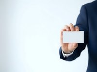 Businessman in dark suit holding blank white card for contact information or branding purposes.