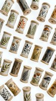 Wooden thread spools decorated with botanical illustrations of ferns, mushrooms, wildflowers, and leaves arranged on white background for craft and sewing projects.