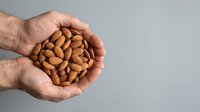 Close-up of hands holding a handful of roasted almonds against neutral background. Suitable for healthy snacking, nutrition, and wellness content.