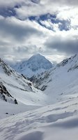 Majestic snow-covered mountain peak rising above pristine winter valley, dramatic clouds casting shadows across untouched powder slopes and rugged alpine terrain.