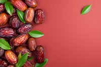 Fresh medjool dates scattered with green leaves on coral red background, creating contrast between natural organic food and solid color surface.