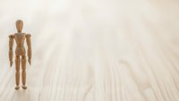 Wooden artist mannequin figure standing on light wood floor surface with copy space for creative design projects and artistic compositions.