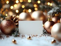 Blank white card mockup with rose gold Christmas ornaments, pine branches and bokeh lights on snowy background. Holiday greeting card design space.