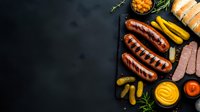 Grilled sausages with pickles, mustard and ketchup sauces on black stone board. Dark food photography with copy space for menu or recipe design.
