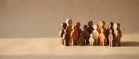 Wooden figures in various skin tones standing together on neutral background, representing diversity, inclusion, community, teamwork, and unity for business and social concepts.